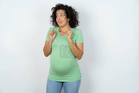 Téléchargez les photos : Femme enceinte serre les poings et attend quelque chose de beau arrivé regarde loin mord lèvres et attend l'annonce des résultats - en image libre de droit
