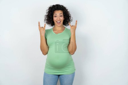Photo for Pregnant woman makes rock n roll sign looks self confident and cheerful enjoys cool music at party. Body language concept. - Royalty Free Image