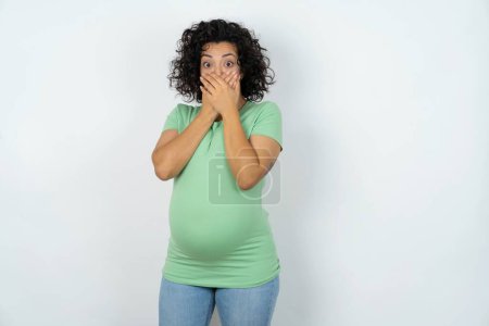 Photo for Stunned pregnant woman covers both hands on mouth, afraids of something astonishing - Royalty Free Image