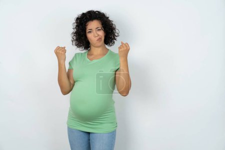 Foto de Mujer embarazada irritada sopla las mejillas con ira y levanta los puños apretados expresa rabia y emociones agresivas. Modelo furioso - Imagen libre de derechos