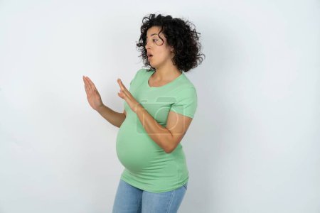 Foto de Mujer embarazada disgustado mantiene las manos hacia el espacio vacío y pide no acercarse ve algo desagradable - Imagen libre de derechos