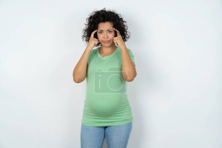 Photo for Serious concentrated pregnant woman keeps fingers on temples, tries to ease tension, gather with thoughts and remember important information for exam - Royalty Free Image