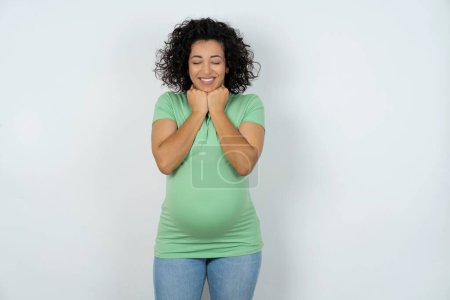Foto de Mujer embarazada alegre tiene expresión satisfecha tímida, sonríe ampliamente, muestra dientes blancos, las emociones de la gente - Imagen libre de derechos