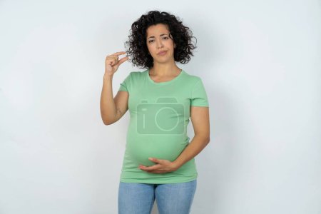 Foto de Mujer embarazada disgustada forma un pequeño letrero de mano demuestra algo no muy grande. Concepto de lenguaje corporal. - Imagen libre de derechos
