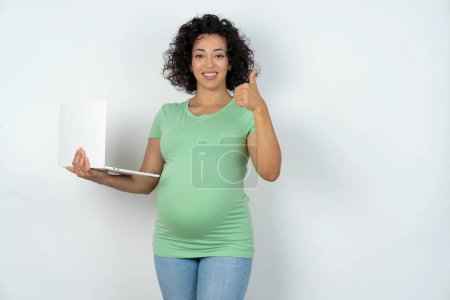 Téléchargez les photos : Belle belle femme enceinte tient netbook et montre pouce vers le haut - en image libre de droit
