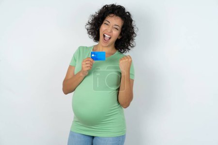 Téléchargez les photos : Excité heureux femme enceinte tenir carte de crédit lever poing dans la victoire - en image libre de droit