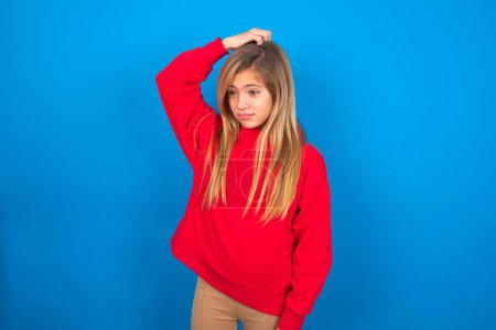 Téléchargez les photos : Belle adolescente caucasienne portant un pull rouge sur un mur bleu disant : Oups, qu'est-ce que j'ai fait ? Tenant la main sur la tête avec une expression effrayée et de regret. - en image libre de droit