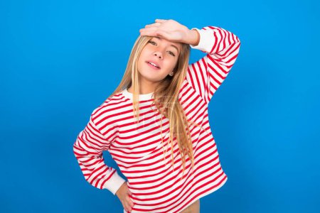 Photo for Beautiful caucasian teen girl wearing striped shirt over blue studio background wiping forehead with hand making phew gesture, expressing relief feels happy that he prevented huge disaster. It was close enough - Royalty Free Image