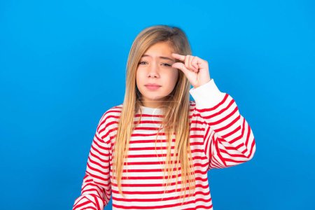 Photo for Upset beautiful caucasian teen girl wearing striped shirt over blue studio background shapes little gesture with hand demonstrates something very tiny small size. Not very much - Royalty Free Image