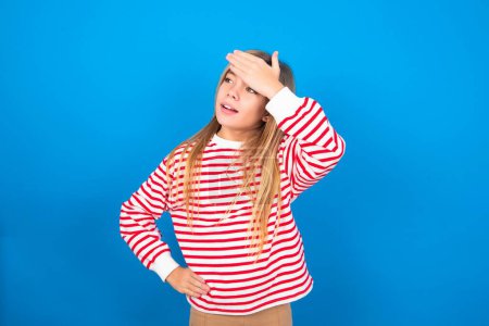 Photo for Beautiful caucasian teen girl wearing striped shirt over blue studio background touching forehead, hears something surprising, glad receive good news, feels relieved. Almost got in trouble. - Royalty Free Image