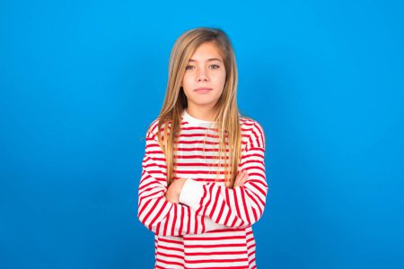 Foto de Foto de enojado hermosa chica adolescente caucásica con camisa a rayas sobre el fondo del estudio azul mirando cámara. - Imagen libre de derechos