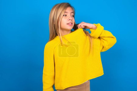 Foto de Hermosa chica adolescente rubia vistiendo suéter amarillo sobre la pared azul estresado, ansioso, cansado y frustrado, tirando del cuello de la camisa, mirando frustrado con el problema - Imagen libre de derechos