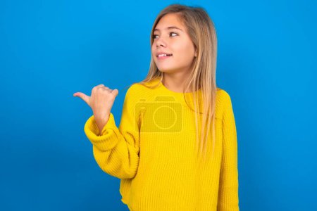 Foto de Hermosa rubia adolescente chica usando amarillo suéter sobre azul de la pared puntos de distancia y da consejos demuestra publicidad - Imagen libre de derechos