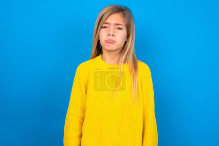 Foto de Hermosa chica adolescente rubia con suéter amarillo sobre la pared azul deprimido y preocuparse por la angustia, llorando enojado y miedo. Expresión triste. - Imagen libre de derechos