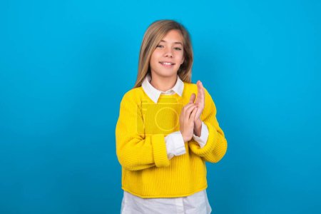 Photo for Caucasian teen girl wearing yellow sweater over blue wall clapping and applauding happy and joyful, smiling proud hands together. - Royalty Free Image