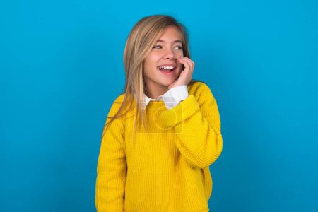 Photo for Caucasian teen girl wearing yellow sweater over blue wall hear incredible private news impressed scream share - Royalty Free Image