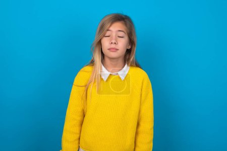 Photo for Caucasian teen girl wearing yellow sweater over blue wall looking sleepy and tired, exhausted for fatigue and hangover, lazy eyes in the morning. - Royalty Free Image