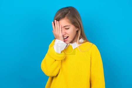 Téléchargez les photos : Adolescent caucasien fille portant un pull jaune sur le mur bleu bâillement fatigué couvrant la moitié du visage, des yeux et de la bouche avec la main. Le visage souffre dans la douleur. - en image libre de droit