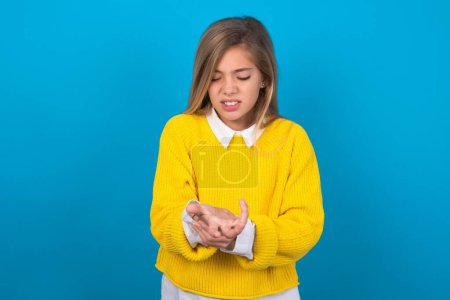 Photo for Caucasian teen girl wearing yellow sweater over blue wall Suffering pain on hands and fingers, arthritis inflammation - Royalty Free Image