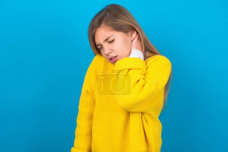 Téléchargez les photos : Adolescent caucasien fille portant un pull jaune sur le mur bleu Souffrant de douleur au cou blessure, toucher le cou avec la main, douleur musculaire - en image libre de droit