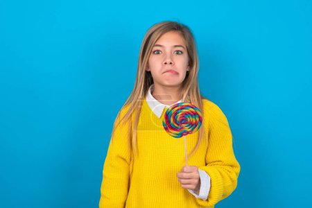 Photo for Caucasian teen girl wearing yellow sweater over blue wall making grimace and crazy face, screaming out of control, funny lunatic expressing freedom and wild. - Royalty Free Image