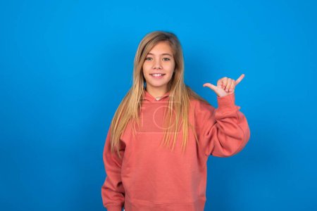 Téléchargez les photos : Belle fille adolescente caucasienne portant un pull rose sur le mur bleu montrant le numéro six Liu avec geste des doigts en langue chinoise signe - en image libre de droit