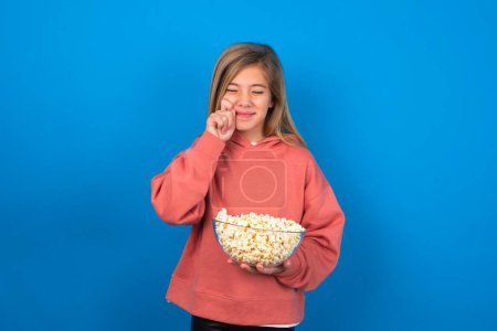 Photo for Pleased beautiful caucasian teen girl wearing pink sweater over blue wall with closed eyes keeps hands near cheeks and smiles tenderly imagines something very pleasant - Royalty Free Image