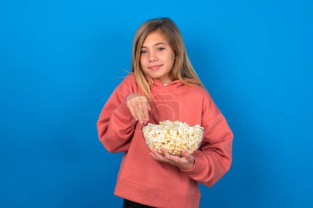 Photo for Beautiful caucasian teen girl wearing pink sweater over blue wall makes bunny paws and looks with innocent expression plays with her little kid - Royalty Free Image