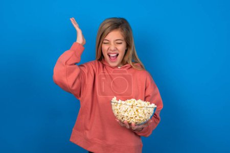 Photo for Beautiful caucasian teen girl wearing pink sweater over blue wall goes crazy as head goes around feels stressed because of horrible situation - Royalty Free Image