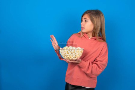 Photo for Displeased beautiful caucasian teen girl wearing pink sweater over blue wall keeps hands towards empty space and asks not come closer sees something unpleasant - Royalty Free Image