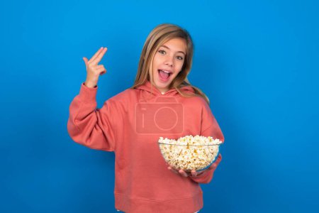 Photo for Beautiful caucasian teen girl wearing pink sweater over blue wall foolishness around shoots in temple with fingers makes suicide gesture. Funny model makes finger gun pistol - Royalty Free Image