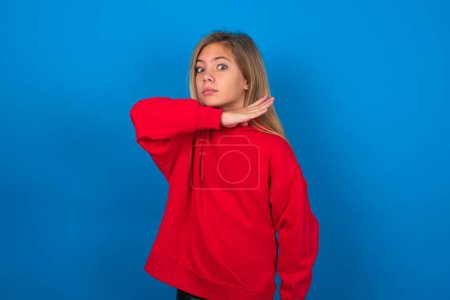 Foto de Rubia adolescente chica usando rojo suéter sobre azul pared cortar garganta con la mano como cuchillo, amenazar la agresión con furiosa violencia. - Imagen libre de derechos