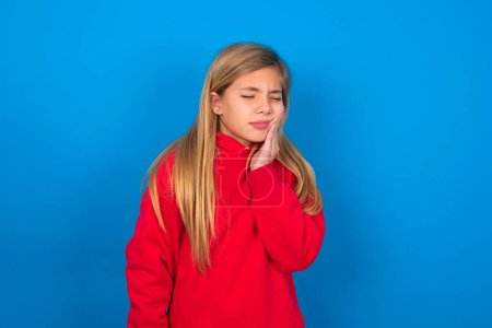 Foto de Rubia adolescente chica usando rojo suéter sobre azul pared con dolor de muelas - Imagen libre de derechos