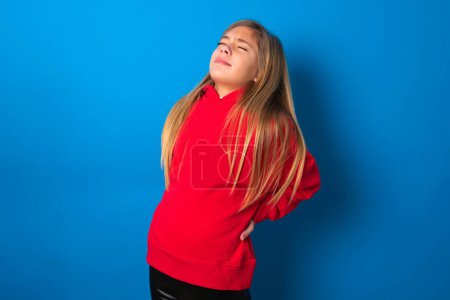 Photo for Blonde teen girl wearing red sweater over blue wall got back pain - Royalty Free Image
