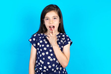 Photo for Nervous puzzled Beautiful kid girl wearing dress over blue background opens mouth from surprise, reacts on sudden news. - Royalty Free Image