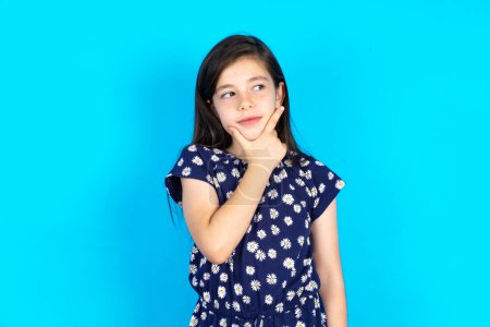 Foto de Hermosa niña con vestido sobre fondo azul Pensando preocupado por una pregunta, preocupado y nervioso con la mano en la barbilla. - Imagen libre de derechos