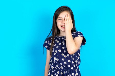 Photo for Beautiful kid girl wearing dress over blue background Covering eyes and mouth with hands, surprised and shocked. Hiding emotions. - Royalty Free Image