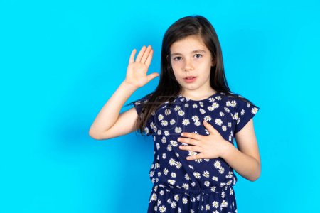 Téléchargez les photos : Belle jeune fille brune caucasienne portant une robe sur fond bleu faisant geste de bonjour avec la main, agitant la main - en image libre de droit