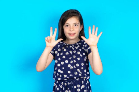 Photo for Beautiful kid girl wearing dress over blue background showing and pointing up with fingers number eight while smiling confident and happy. - Royalty Free Image