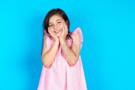 Photo for Inspired Beautiful kid girl wearing pink dress over blue background looking at copyspace having thoughts about future events - Royalty Free Image