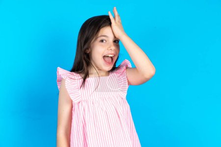 Photo for Beautiful kid girl wearing pink dress over blue background surprised with hand on head for mistake, remember error. Forgot, bad memory concept. - Royalty Free Image