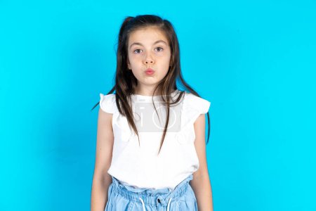 Photo for Shot of pleasant looking kid, pouts lips, looks at camera, Human facial expressions. Beautiful caucasian little girl posing over blue studio background - Royalty Free Image