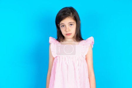 Photo for Displeased upset kid frowns face as going to cry, being discontent and unhappy as can't achieve goals,  Disappointed model has troubles. Beautiful caucasian little girl posing over blue studio background - Royalty Free Image