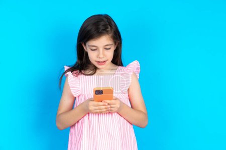 Photo for Kid using mobile phone chatting . Beautiful caucasian little girl posing over blue studio background - Royalty Free Image