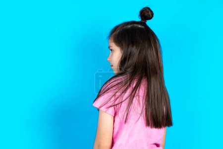 Téléchargez les photos : La vue de derrière d'un enfant. Studio Shoot. Belle petite fille caucasienne posant sur fond bleu studio - en image libre de droit