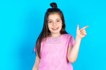 Foto de Niño apuntando hacia arriba con los dedos número ocho en chino lenguaje de signos B. Hermosa niña caucásica posando sobre fondo de estudio azul - Imagen libre de derechos