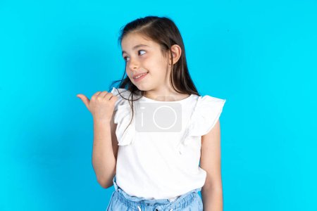 Foto de Kid señala y demuestra publicidad. Hermosa niña caucásica posando sobre fondo de estudio azul - Imagen libre de derechos