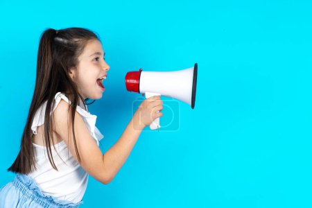 Photo for Funny kid screaming in megaphone. People sincere emotions lifestyle concept. Mock up with copy space. Beautiful caucasian little girl posing over blue studio background - Royalty Free Image