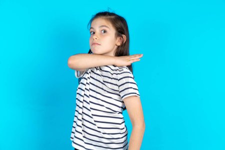 Photo for Kid cutting throat with hand as knife, threaten aggression with furious violence. Beautiful caucasian girl standing over blue studio background - Royalty Free Image