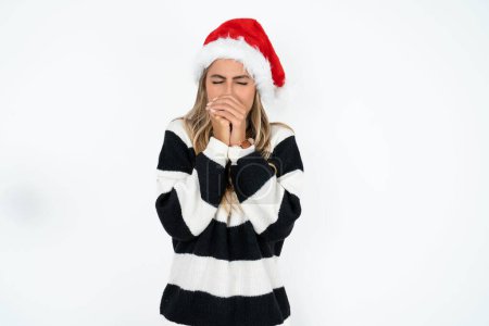 Foto de Joven mujer caucásica vistiendo sombrero de Santa y suéter a rayas contra fondo de estudio blanco sosteniéndose, se siente muy frío afuera, esperanzas que no se enfriarán - Imagen libre de derechos